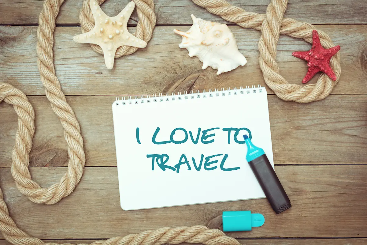 'I LOVE TO TRAVEL' message on notepad with nautical rope and shells on wooden background