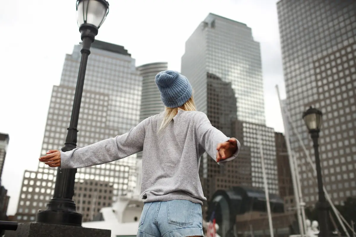 Woman with arms outstretched facing modern city skyscrapers