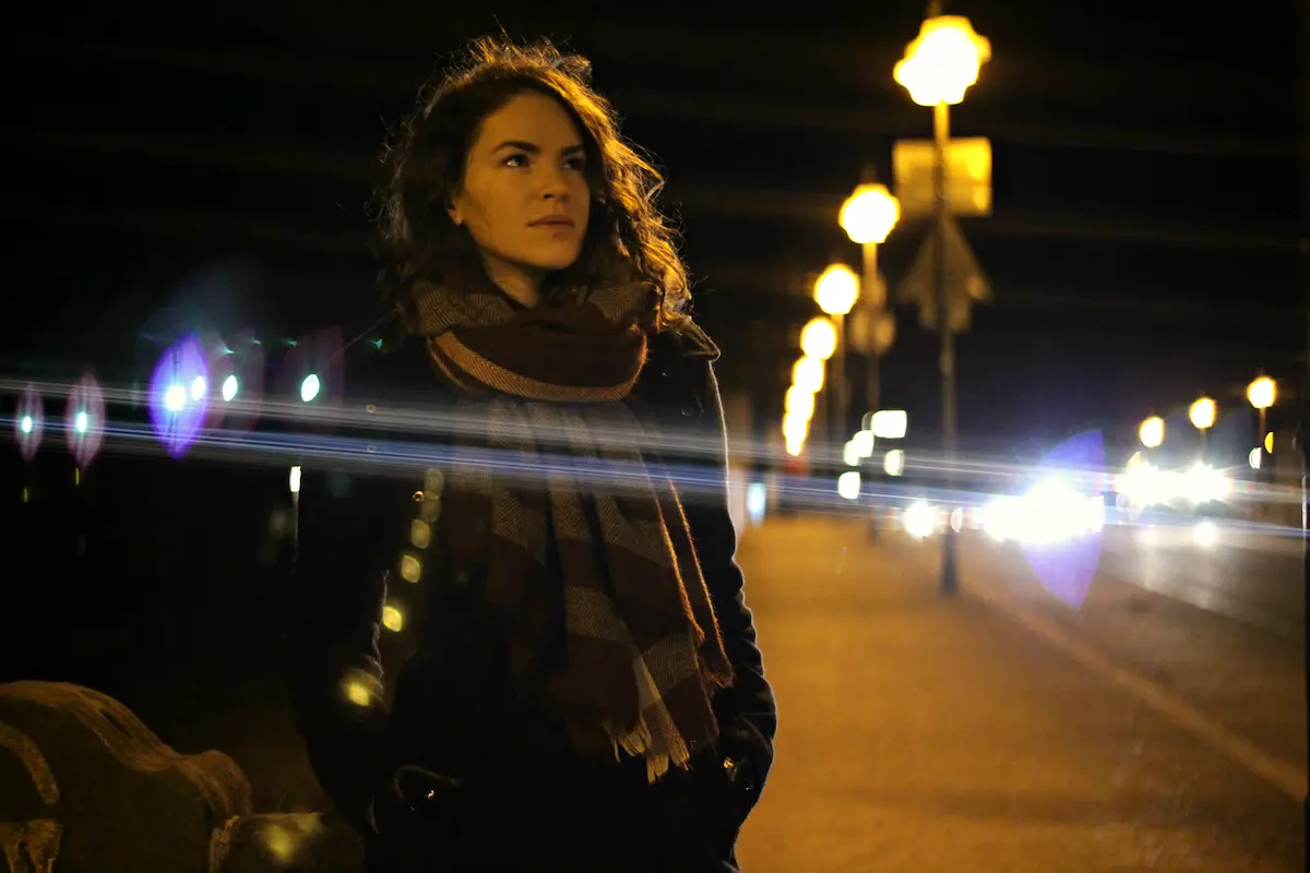 Woman in scarf looks over shoulder on city street at night