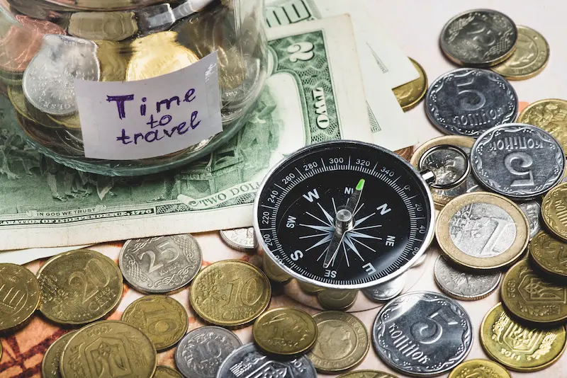 'Time to travel' savings jar with compass, coins, and dollar bills