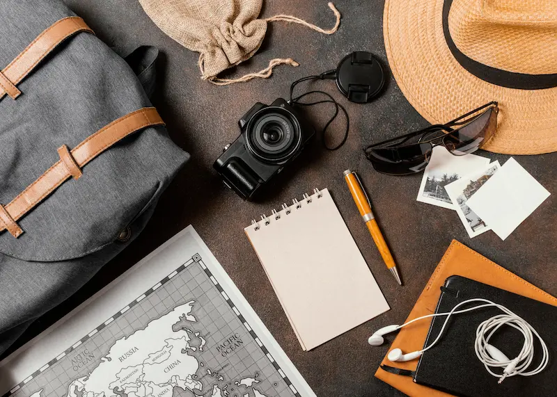 Travel planning flat lay with map, camera, notepad, hat, and backpack