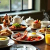 Breakfast spread with bacon, eggs, pastries, orange juice and tea on wooden table by window