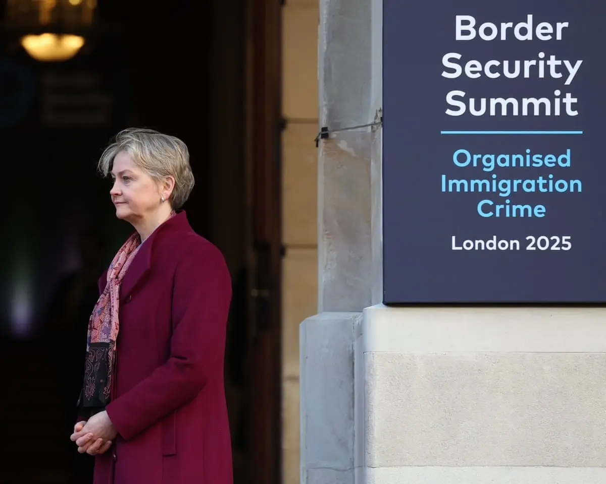 Yvette Cooper standing next to a "Border Security Summit, Organised Immigration Crime, London 2025" sign