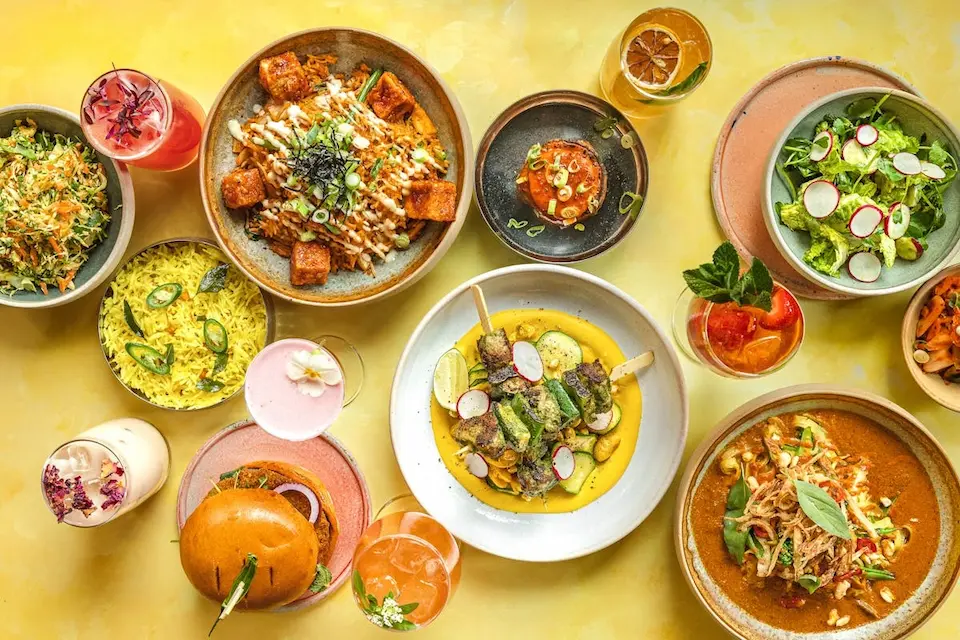 An overhead view of a colourful spread of vegan dishes and cocktails from one of the best vegan restaurants London has to offer
