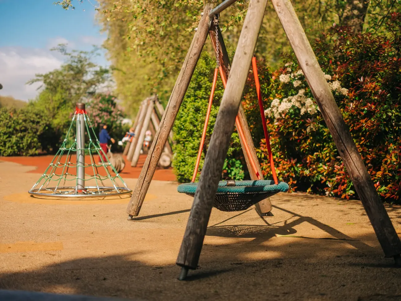 Wooden basket swing in a sunny park playground with climbing frame behind
