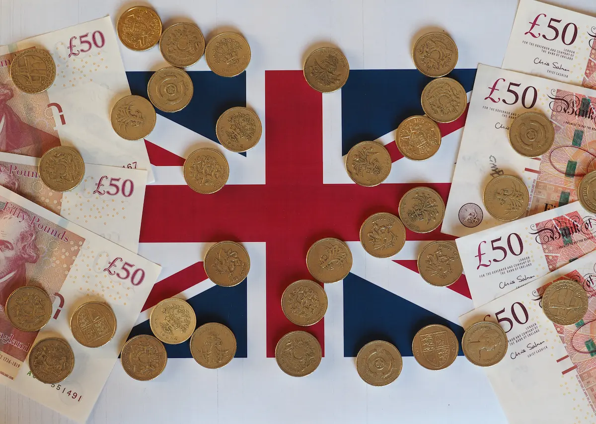 UK Union Jack flag partially covered with fifty pound notes and one pound coins