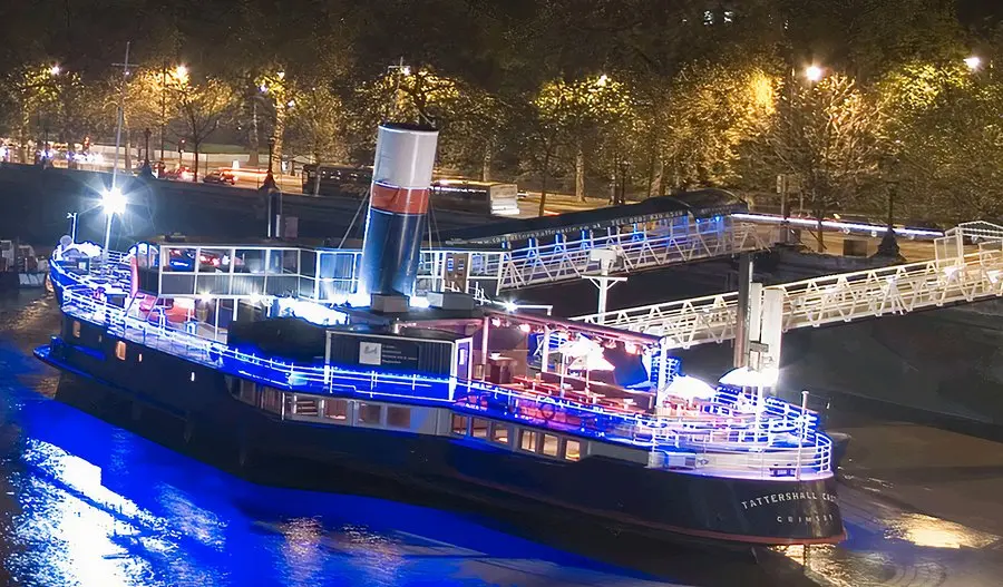 The Tattershall Castle boat moored on the Thames at night, illuminated with bright blue lights