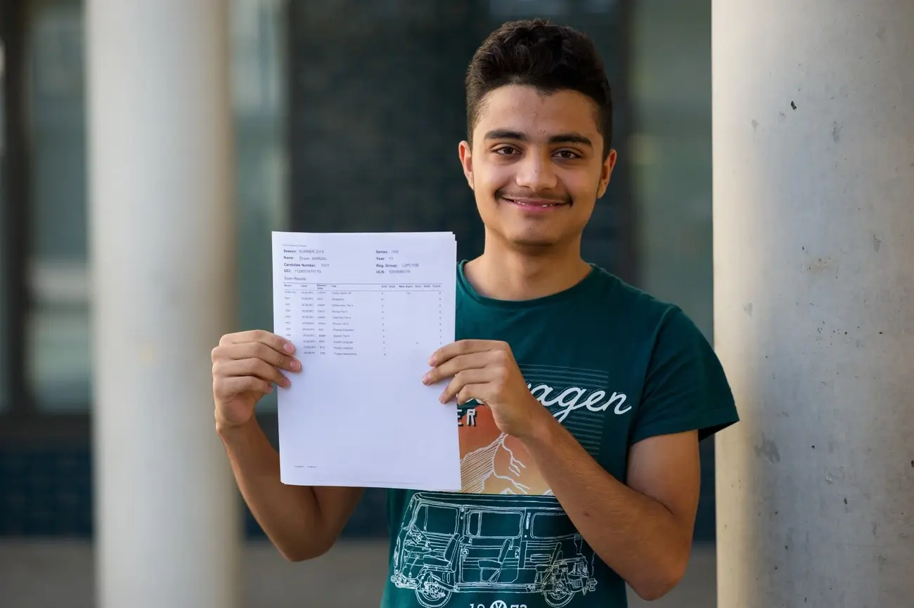 Young male student in a green t-shirt smiling and proudly displaying his exam results certificate