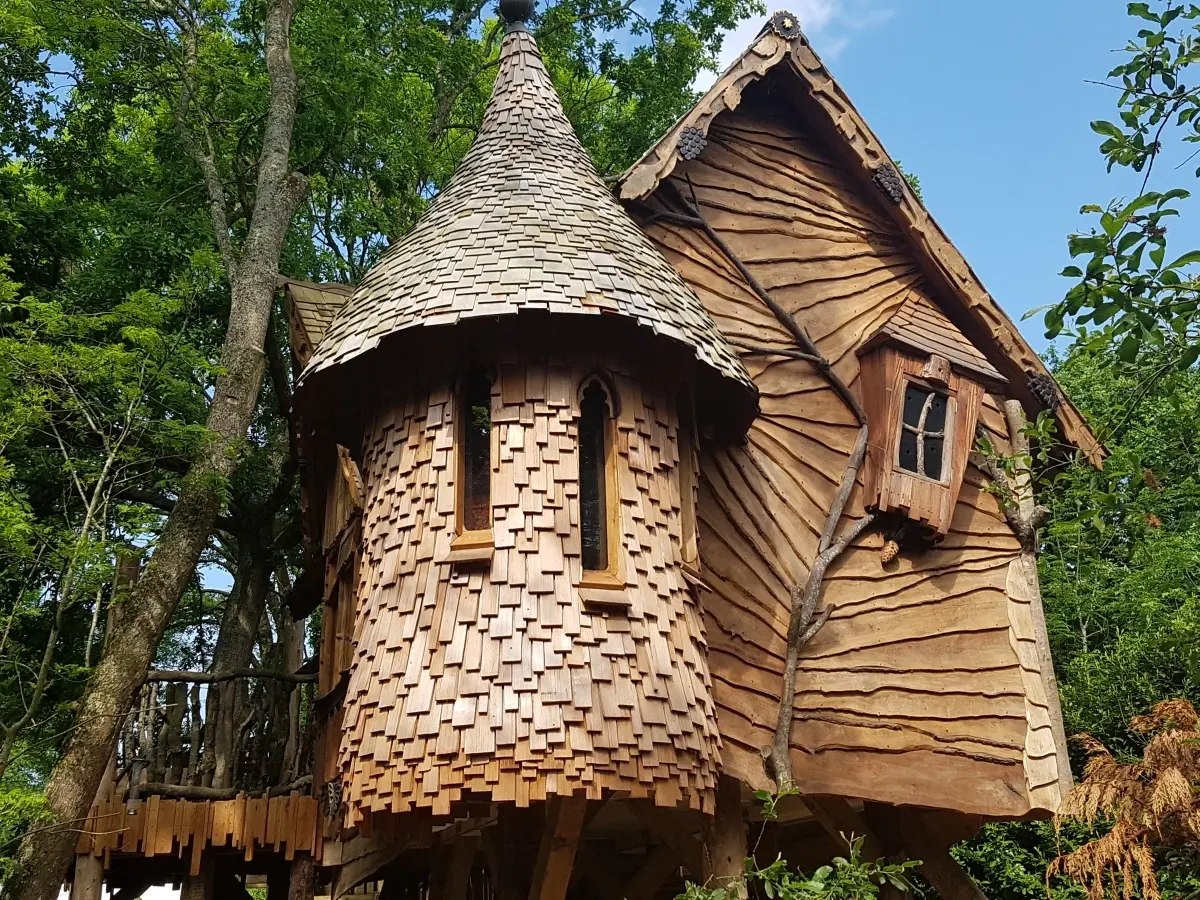 Unique wooden shingled treehouse at Blackberry Wood with a whimsical turret design, nestled in a forest