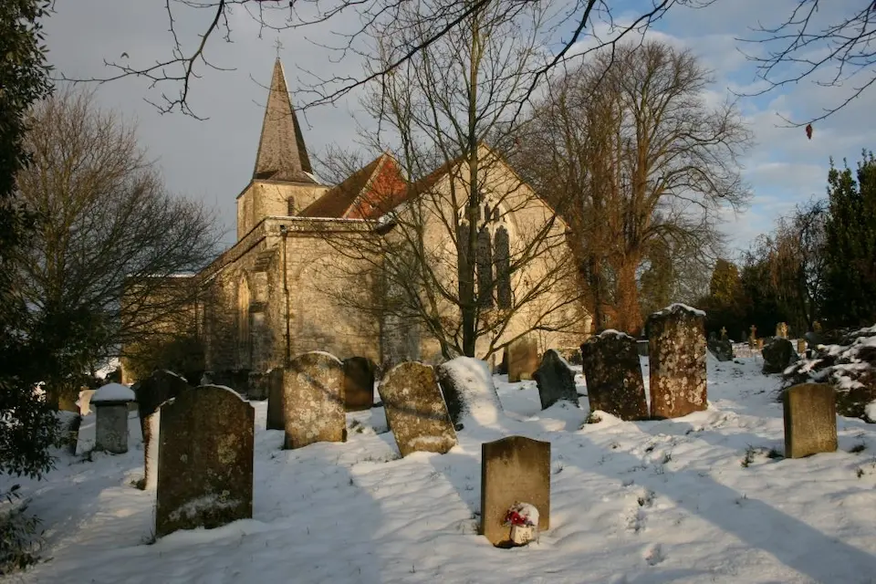 St Nicholas Church in Pluckley village, Kent, seen across its graveyard covered in snow under a winter sky