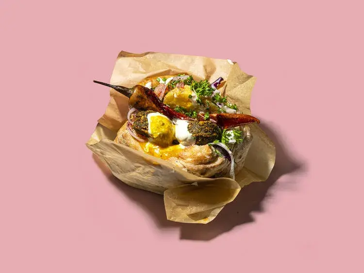 A close-up of a freshly made falafel pita from Pockets, wrapped in paper with a chilli on top