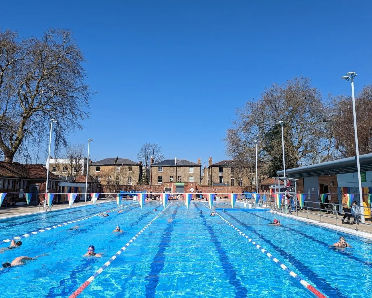 People swimming laps in the sunny London Fields Lido, a popular outdoor pool in one of Hackney's best Parks in London