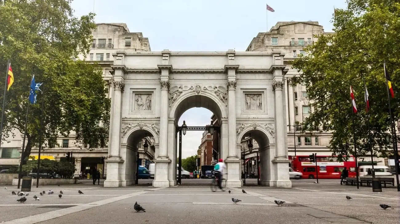 London's Marble Arch monument on a bright day, with pigeons in the foreground and a red double-decker bus passing