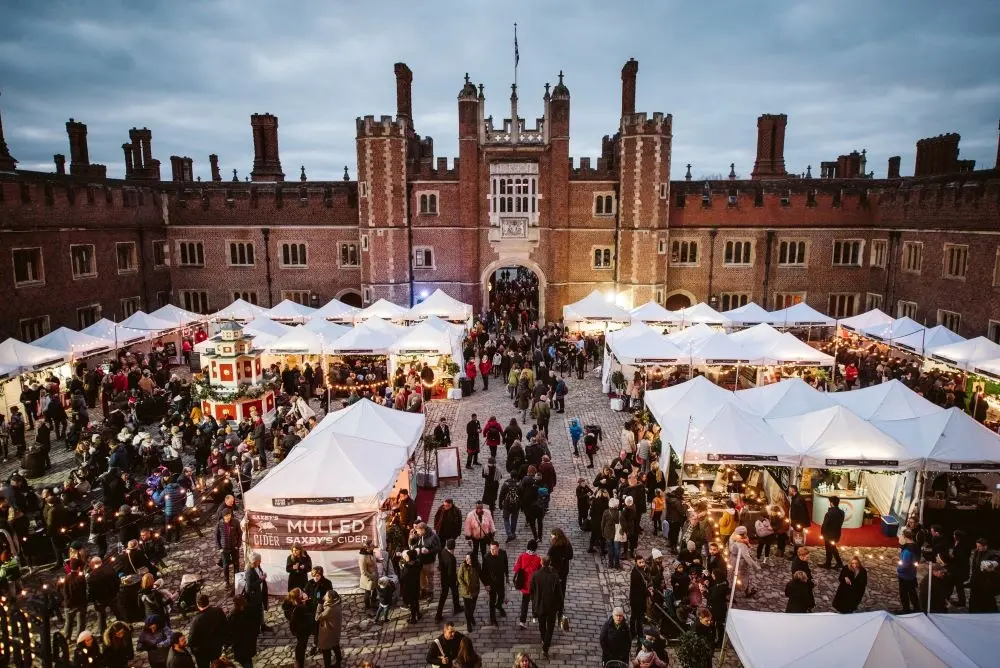 An overhead view of the busy Hampton Court Palace Festive Fayre, with crowds browsing white-tented stalls in the historic courtyard