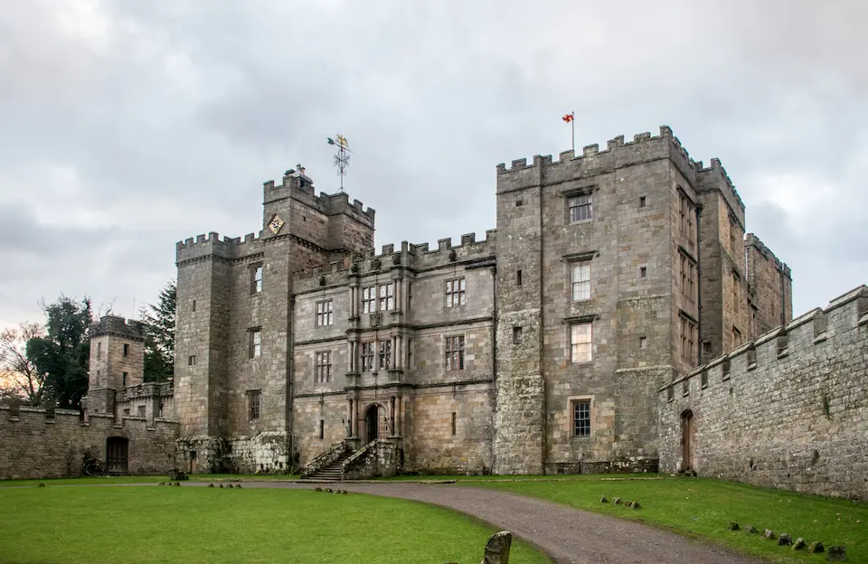 Exterior view of the imposing stone Chillingham Castle in Northumberland under a cloudy sky