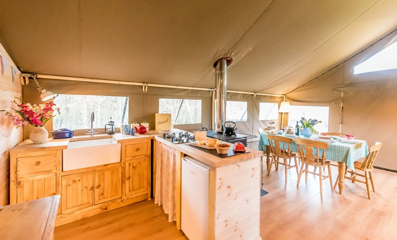 Well-equipped kitchen and dining area inside a Shillingridge Glamping safari tent lodge, showing a sink, cooker, and table
