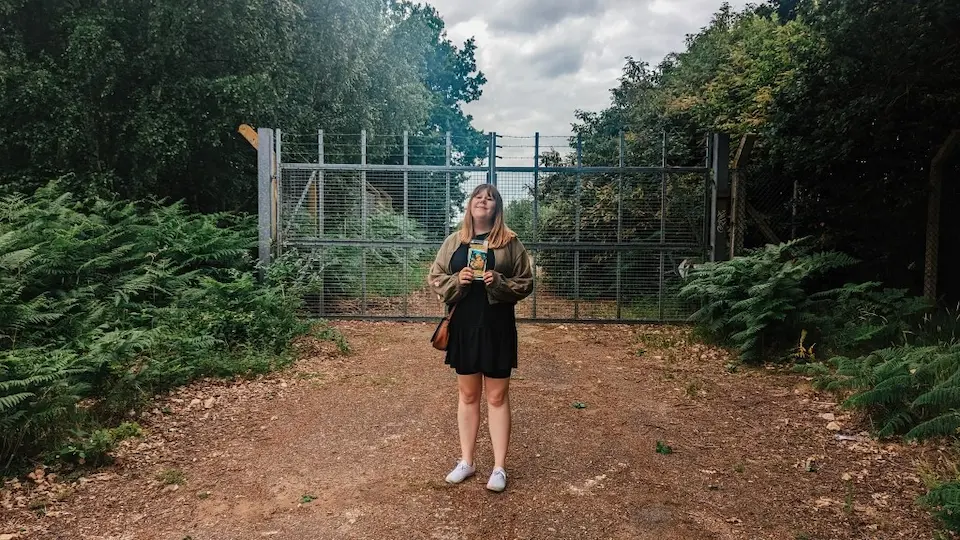 Person standing on a dirt path before a large metal gate at an entrance to Rendlesham Forest, Suffolk