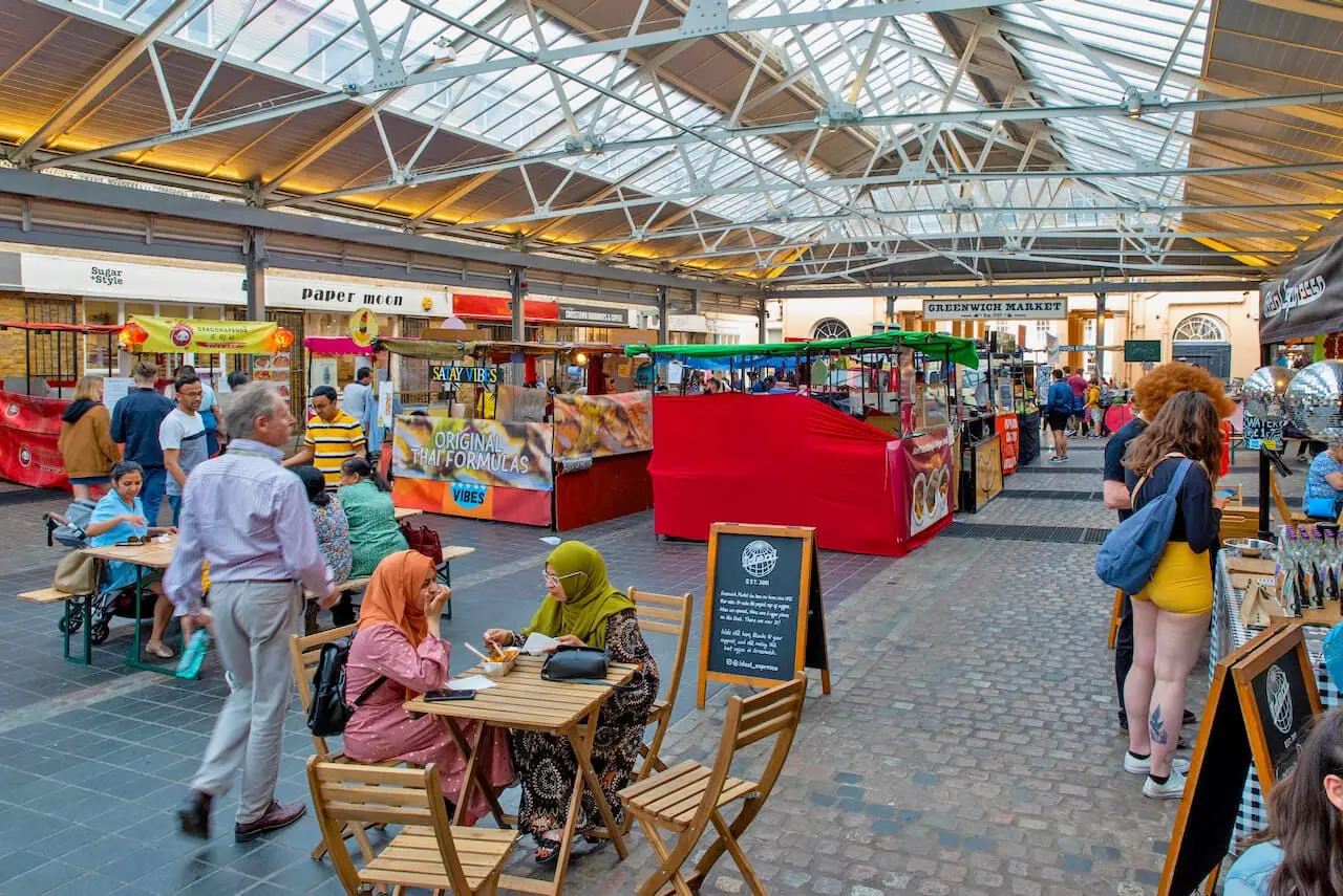 View inside Greenwich Market showing food stalls and people eating at tables under the covered roof