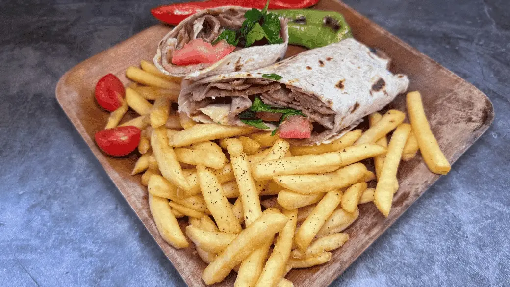 EaTurkish doner kebab wrap served with chips on a wooden board