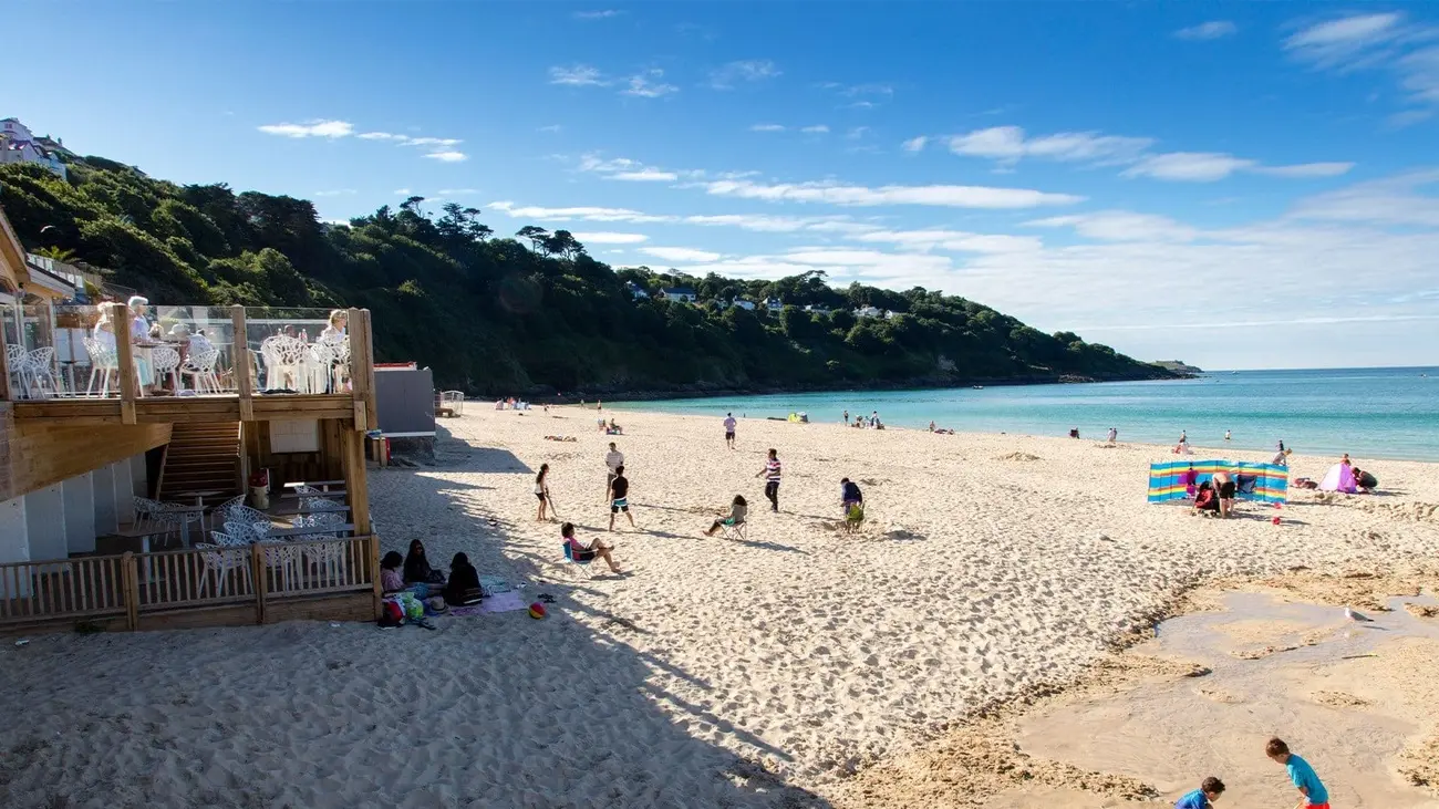 People enjoying the golden sand at Carbis Bay beach, Cornwall, with beach cafe on left