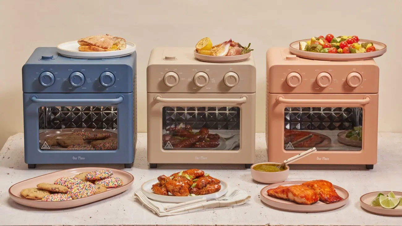 Three Our Place Wonder Ovens in different colours surrounded by cooked food
