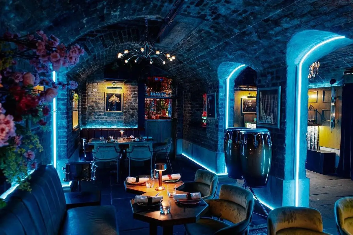 Moodily lit interior of Cache Cache London, a hidden speakeasy bar with blue neon accents and plush seating