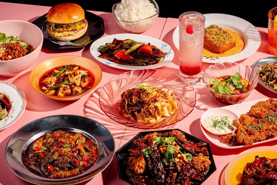 A vibrant table spread of Chinese fusion dishes, including noodles and a burger, at Facing Heaven
