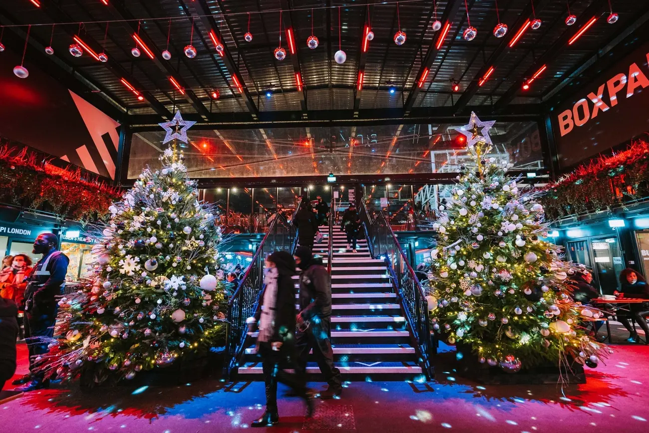 The interior of Boxpark Croydon decorated for Christmas, with two large, brightly lit Christmas trees flanking a central staircase