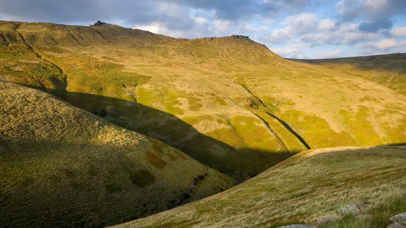 Sunlight hitting the grassy slopes of Kinder Scout under a cloudy sky