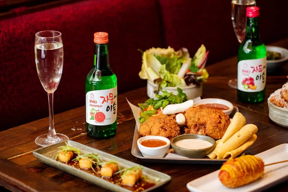 Assortment of Korean Dinner Party brunch dishes including fried chicken, tacos, and Jinro Soju