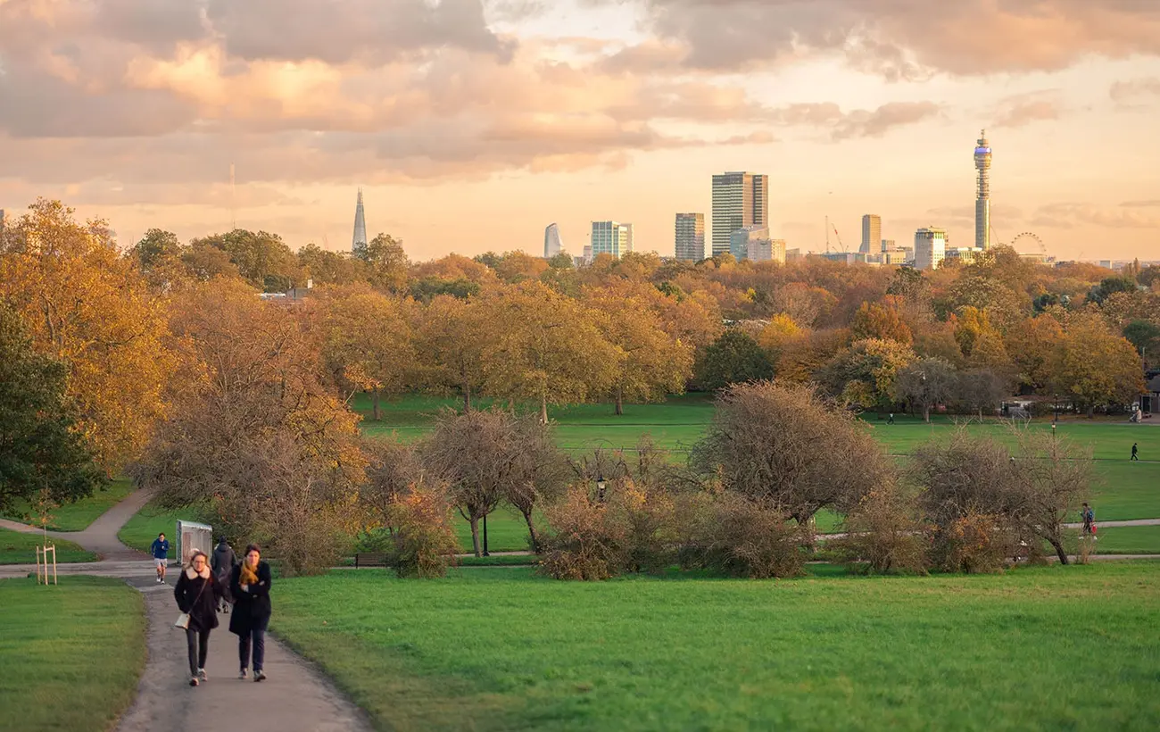 Two people walking on path in Primrose Hill, one of the scenic Parks in London, with skyline at dusk