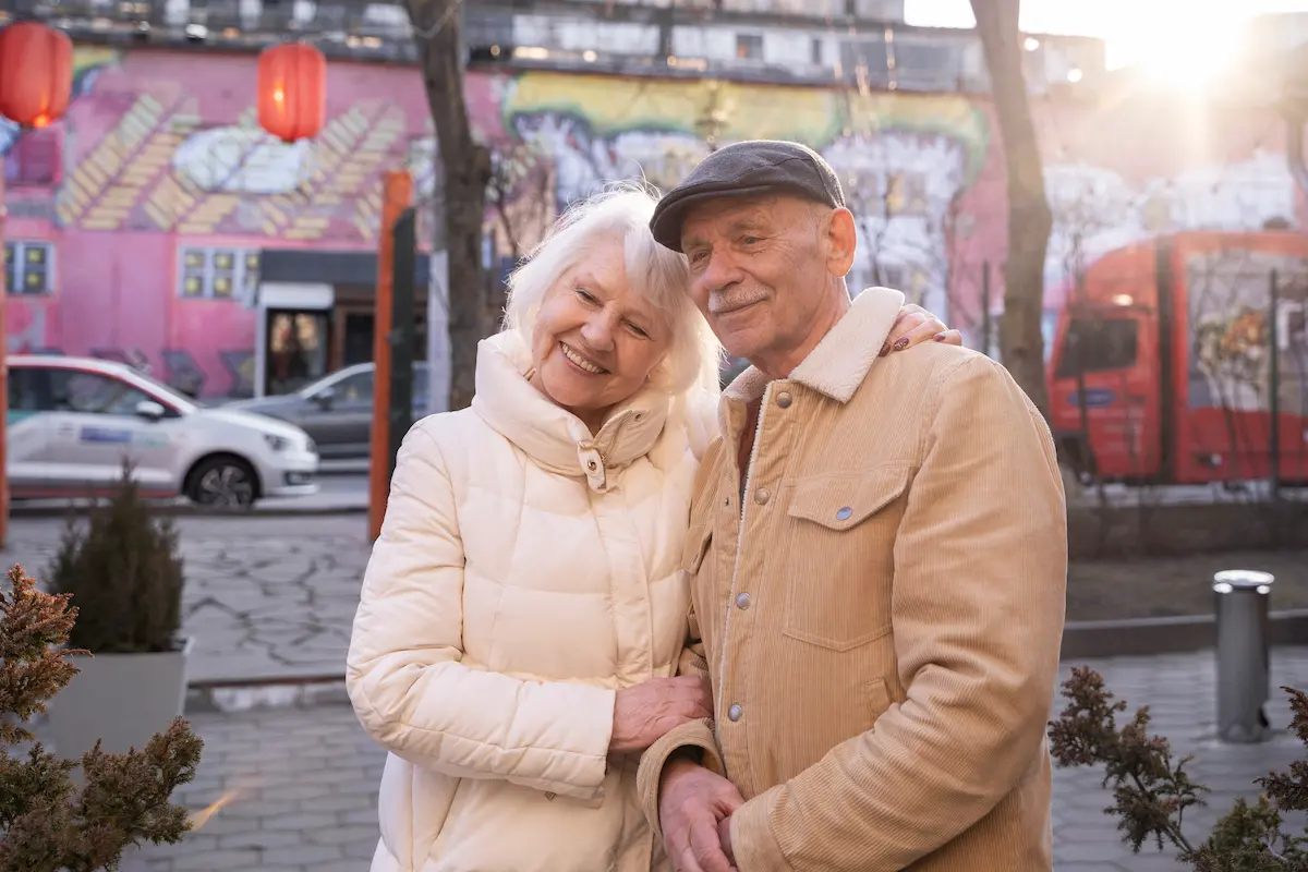 Smiling senior couple wearing coats and embracing outdoors on a sunny day