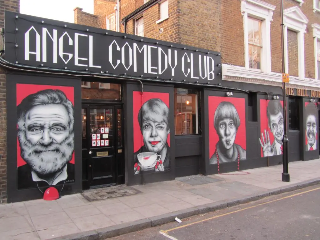 Exterior street view of The Bill Murray pub, home to Angel Comedy Club, with large comedian portraits on the facade