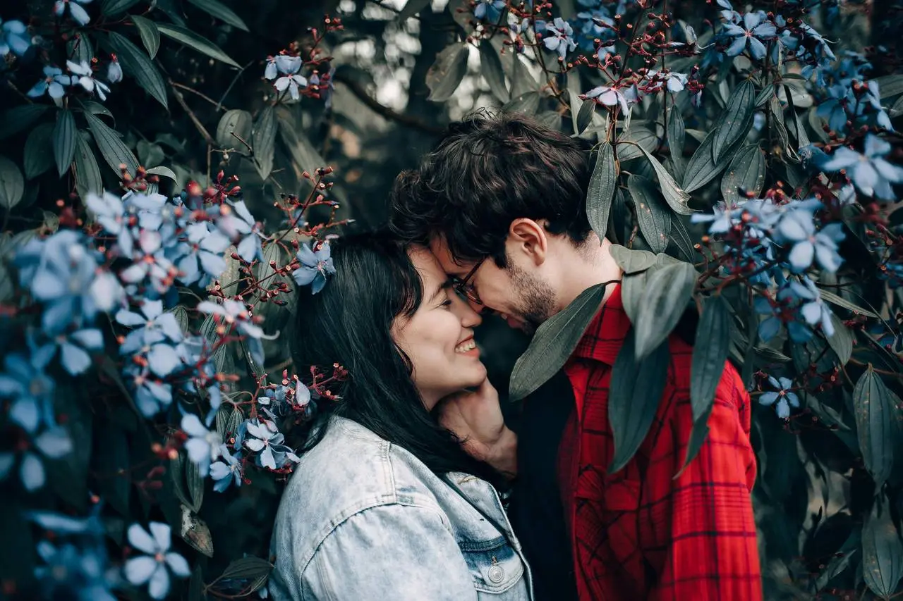 Young couple smiling and touching foreheads intimately outdoors among blue flowers