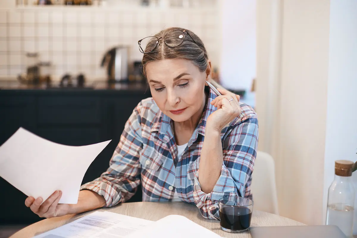 Woman sitting at a kitchen table carefully reviewing paperwork