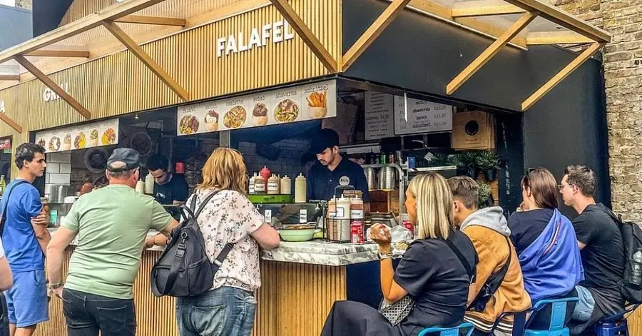 Customers ordering and eating at the Basta falafel stall counter in Camden Market