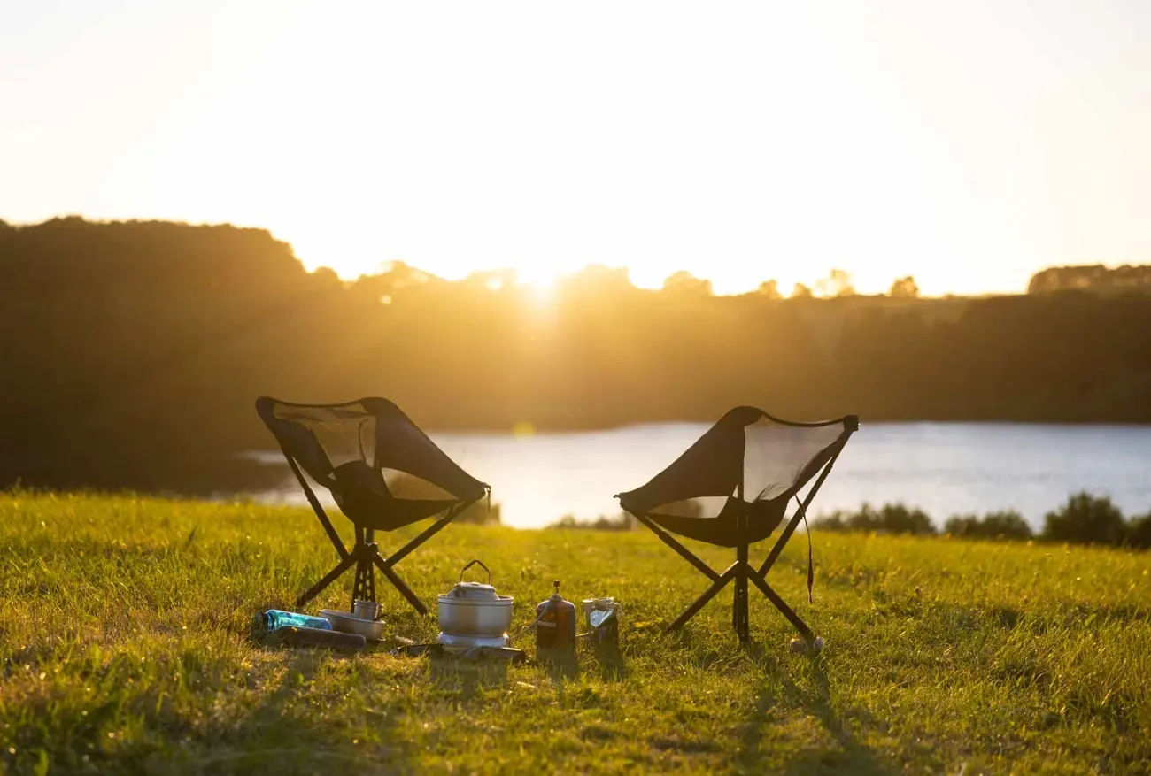 Two Sitpack Campster 2 chairs on grassy hill overlooking a lake at sunset