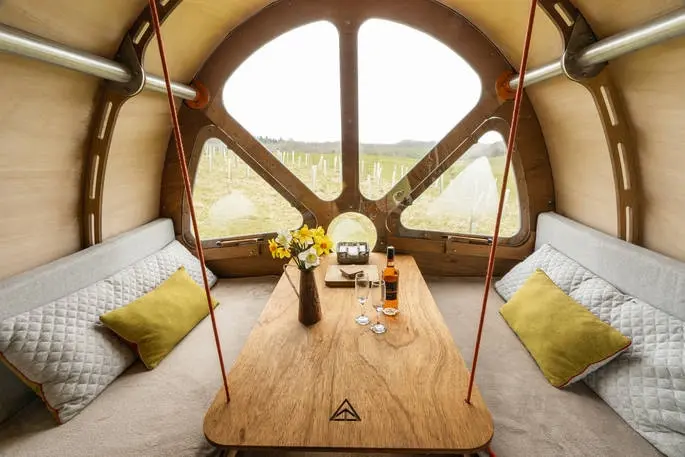 Interior of Hedgehog Hall glamping pod showing a wooden table, seating, and a large window with countryside views