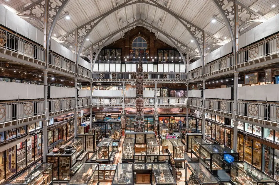 Wide interior view of the Pitt Rivers Museum, showing multiple floors with balconies packed with glass display cases
