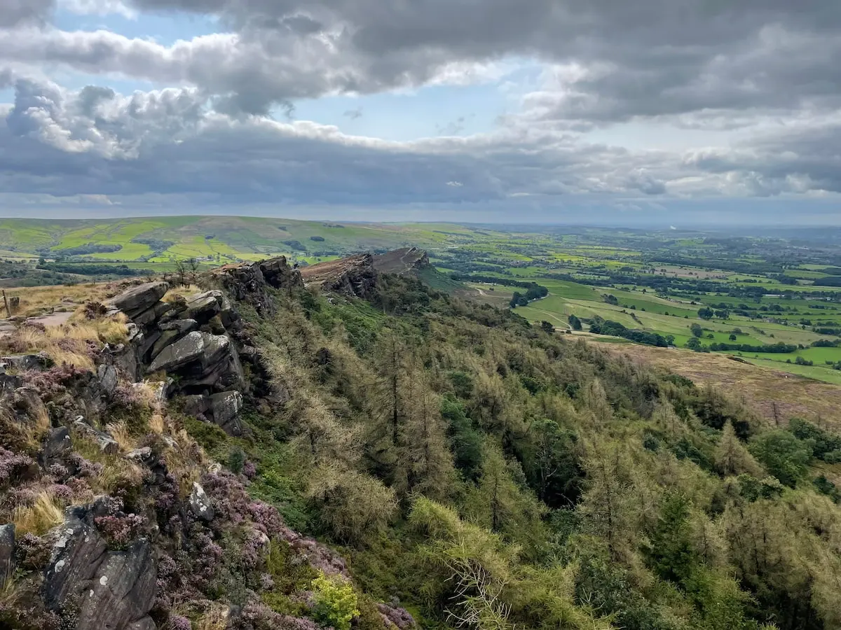 View from The Roaches ridge looking over rocky outcrops and green fields under a cloudy sky