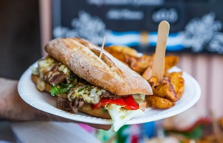Hand holding paper plate with large Argentine steak sandwich and potato wedges