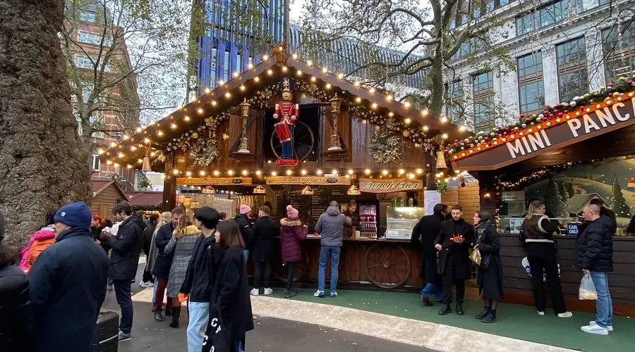 People queuing at a festive wooden stall selling mini pancakes and French fries at the Leicester Square Christmas Market