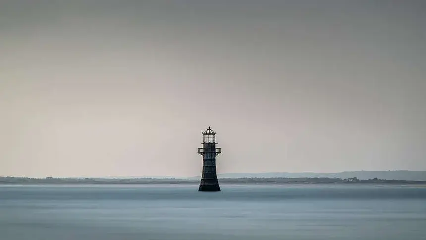 The isolated cast-iron Whiteford Lighthouse standing in the calm sea under a grey, overcast sky