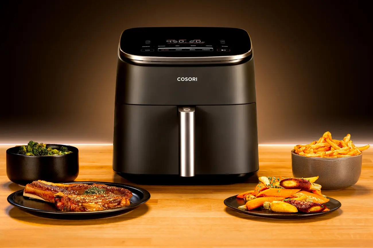 Black Cosori TurboBlaze air fryer surrounded by plates of cooked steak, fries, and vegetables