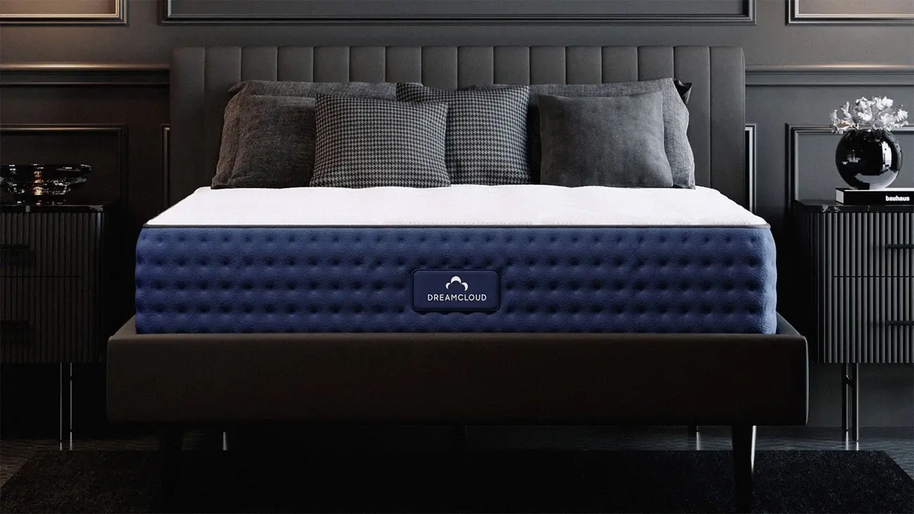 DreamCloud Luxury Hybrid mattress on a dark bed frame in a moody bedroom setting