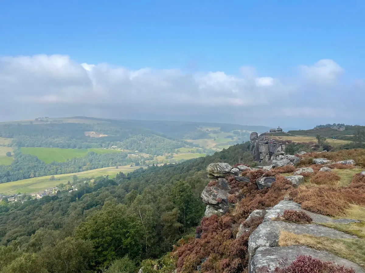 View along the rocky Curbar Edge with heather overlooking distant hills