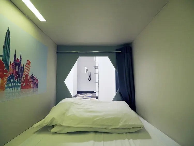 Interior view of a compact St. Christopher's Inn capsule pod with a bed and travel-themed wall art