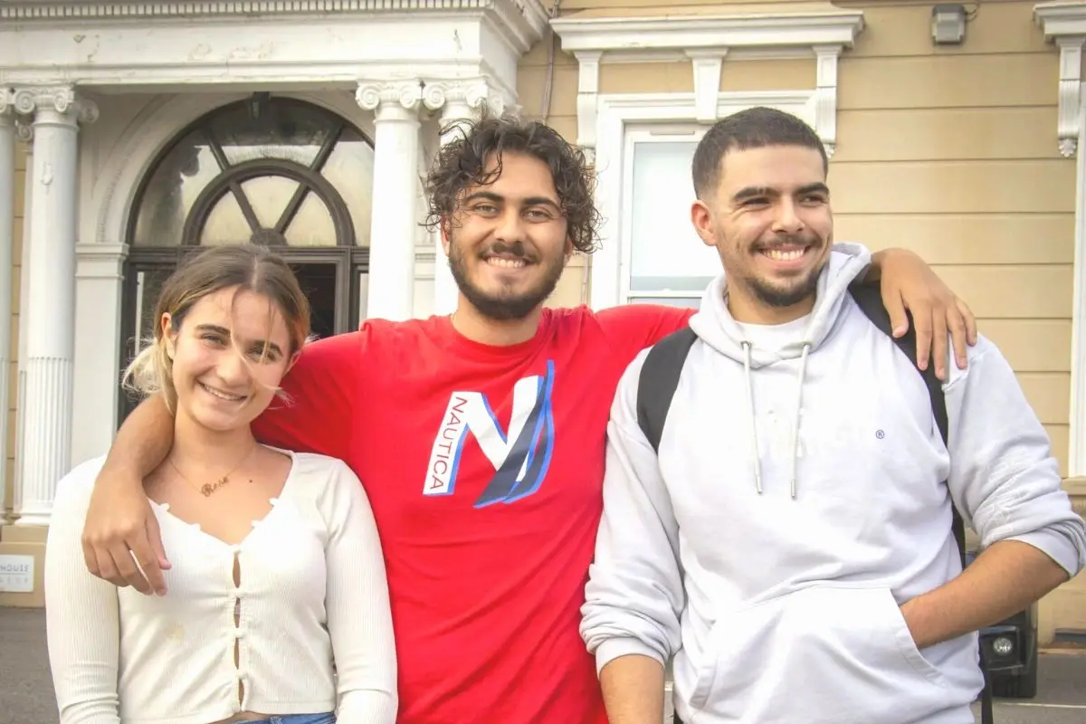 Three smiling Woodhouse College students with arms around each other in front of the college building