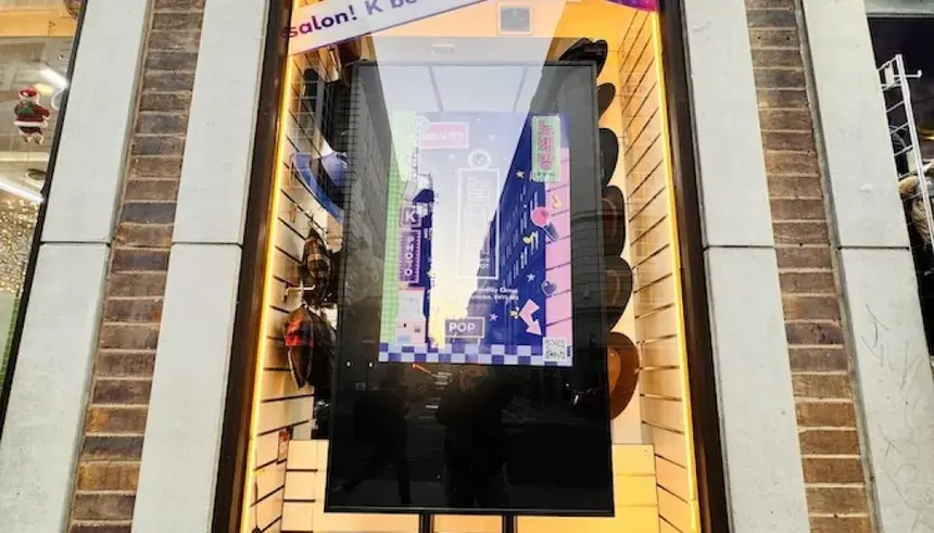 A large, vertical digital screen in the window of K-Pop Playground, showing a vibrant, neon-style K-pop graphic