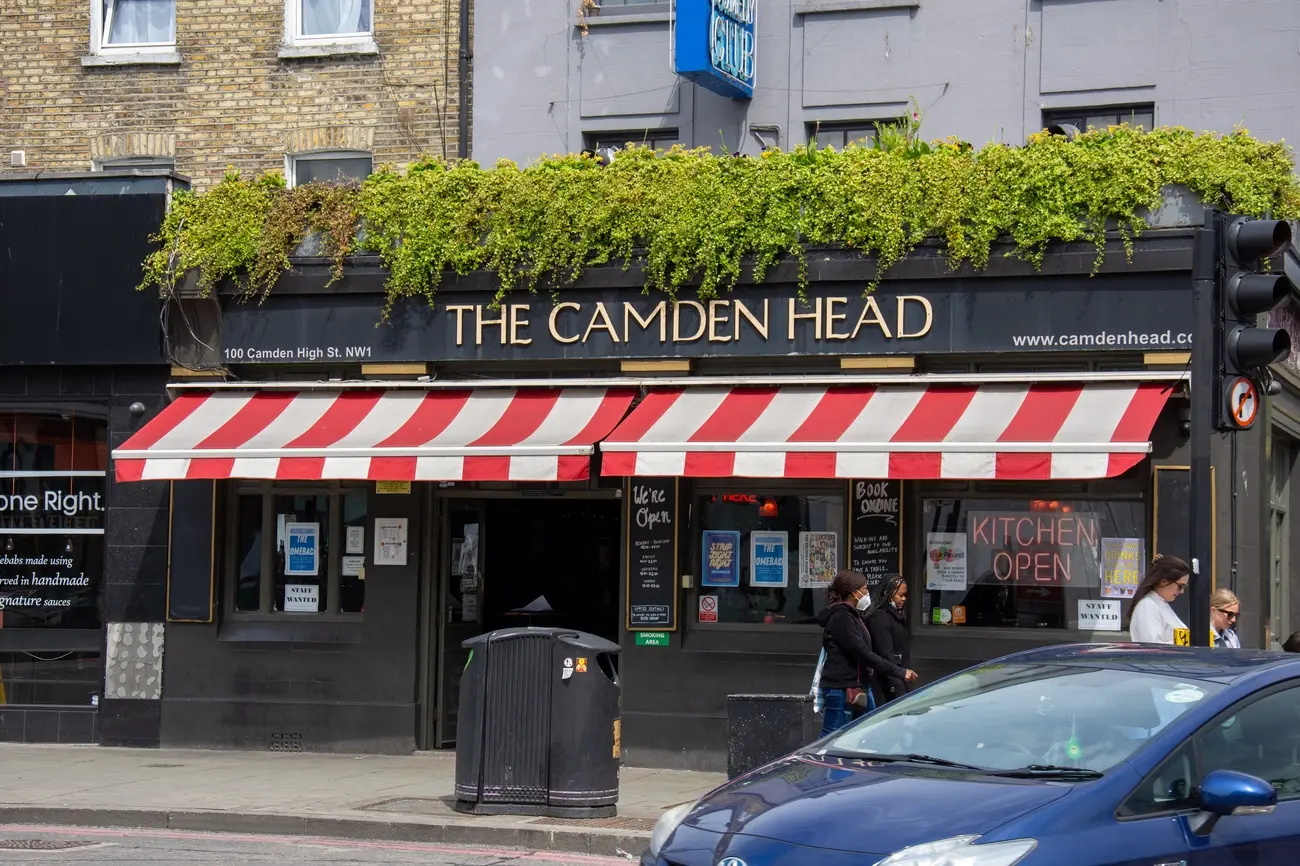 Street view of The Camden Head pub exterior in Camden, showing the facade with red and white striped awnings